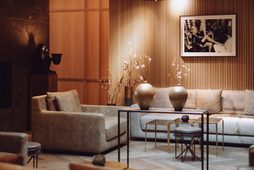 Sitzbereich in einer Hotellobby mit Sofas, Tischen, Holzverkleidung und runden Deckenleuchten.