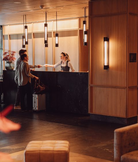 Gast beim Check-in an der Rezeption in einer warm beleuchteten Hotellobby.