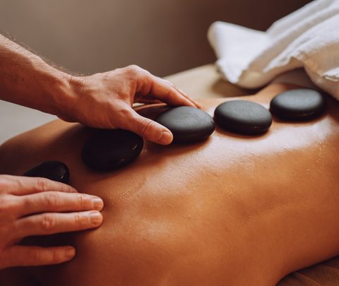 Hände platzieren warme Massagesteine auf den Rücken einer liegenden Person bei einer Hot-Stone-Massage.