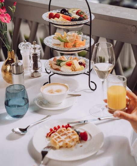 Gedeckter Restauranttisch mit Frühstücks-Etagere, Cappuccino, Waffel, Orangensaft und einem Glas Sekt.
