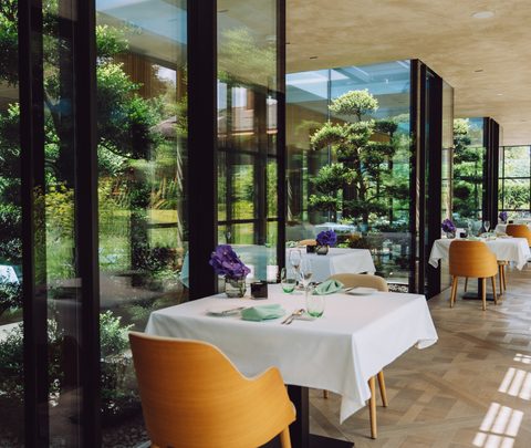 Restaurant with white-clothed tables beside a large window front overlooking the garden.