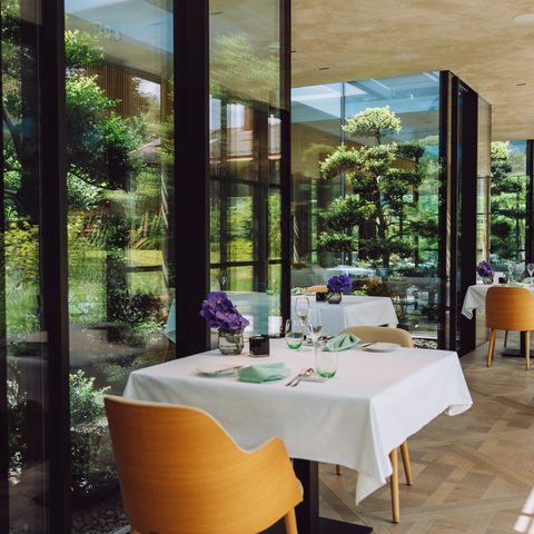Restaurant mit weiß gedeckten Tischen an einer großen Fensterfront mit Blick in den Garten.