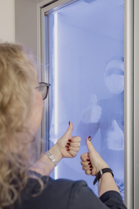 Eine Frau zeigt vor einer blau beleuchteten Kältekammer beide Daumen nach oben.