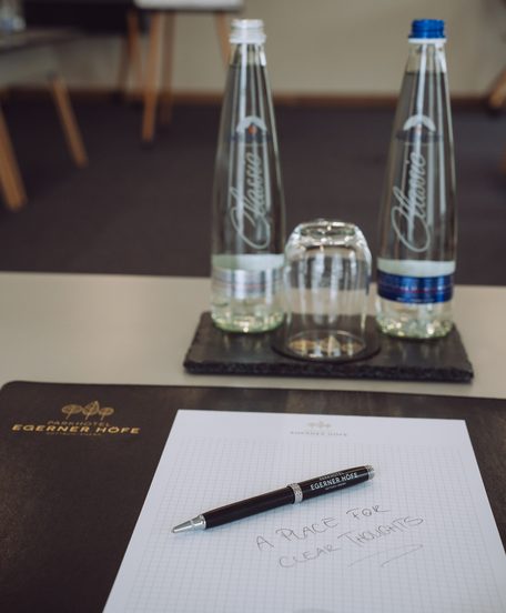 Seminartisch mit zwei Wasserflaschen, Glas, Notizblock und Stift in einem Tagungsraum.