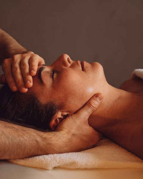 Eine Frau erhält eine Gesichts- und Nackenmassage auf einer Liege im Wellnessbereich.