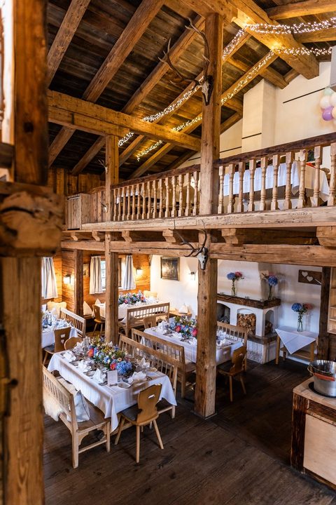 Rustikaler Restaurantbereich mit gedeckten Tischen, Holzbalken und offener Galerie in einer Stube.