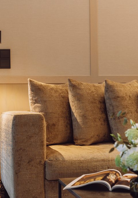 Wohnbereich einer Hotelsuite mit Sofa, Couchtisch und Blick durch den Durchgang ins Badezimmer.