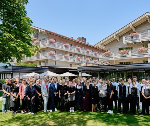 Hotel team poses for a group photo in the garden in front of the hotel building.