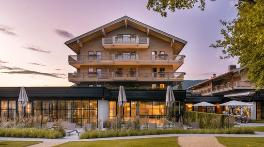 Exterior of a hotel with balconies, terrace, and garden at dusk.