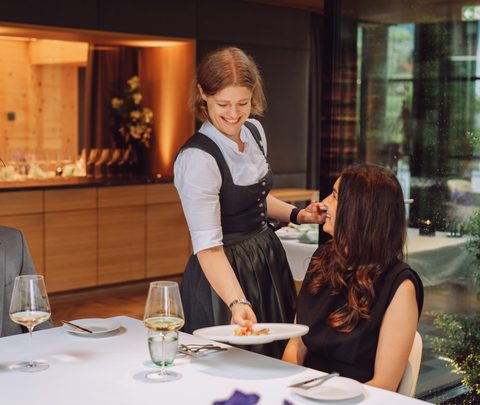 Eine Kellnerin serviert einem Paar das Essen an einem gedeckten Tisch im Restaurant.
