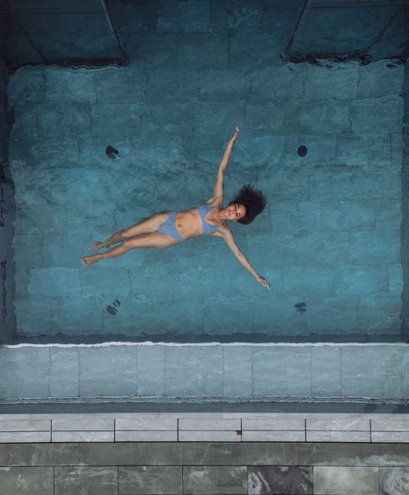 Eine Frau treibt auf dem Rücken in einem rechteckigen Pool, aufgenommen aus der Draufsicht.