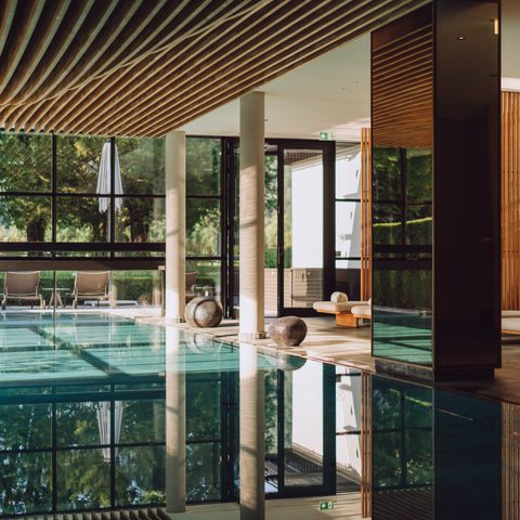 Indoor pool in the wellness area with lounge chairs, large windows and wooden ceiling.