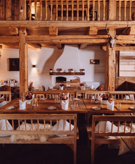 Rustikaler Restaurantbereich mit gedeckten Holztischen, Kamin und Galerie aus Altholz.
