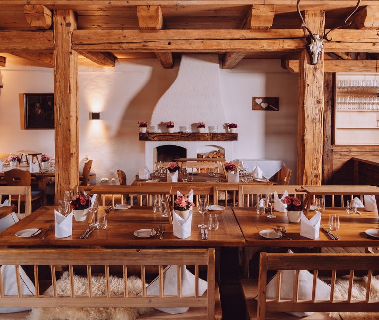 Rustikaler Restaurantbereich mit gedeckten Holztischen, Kamin und Galerie aus Altholz.